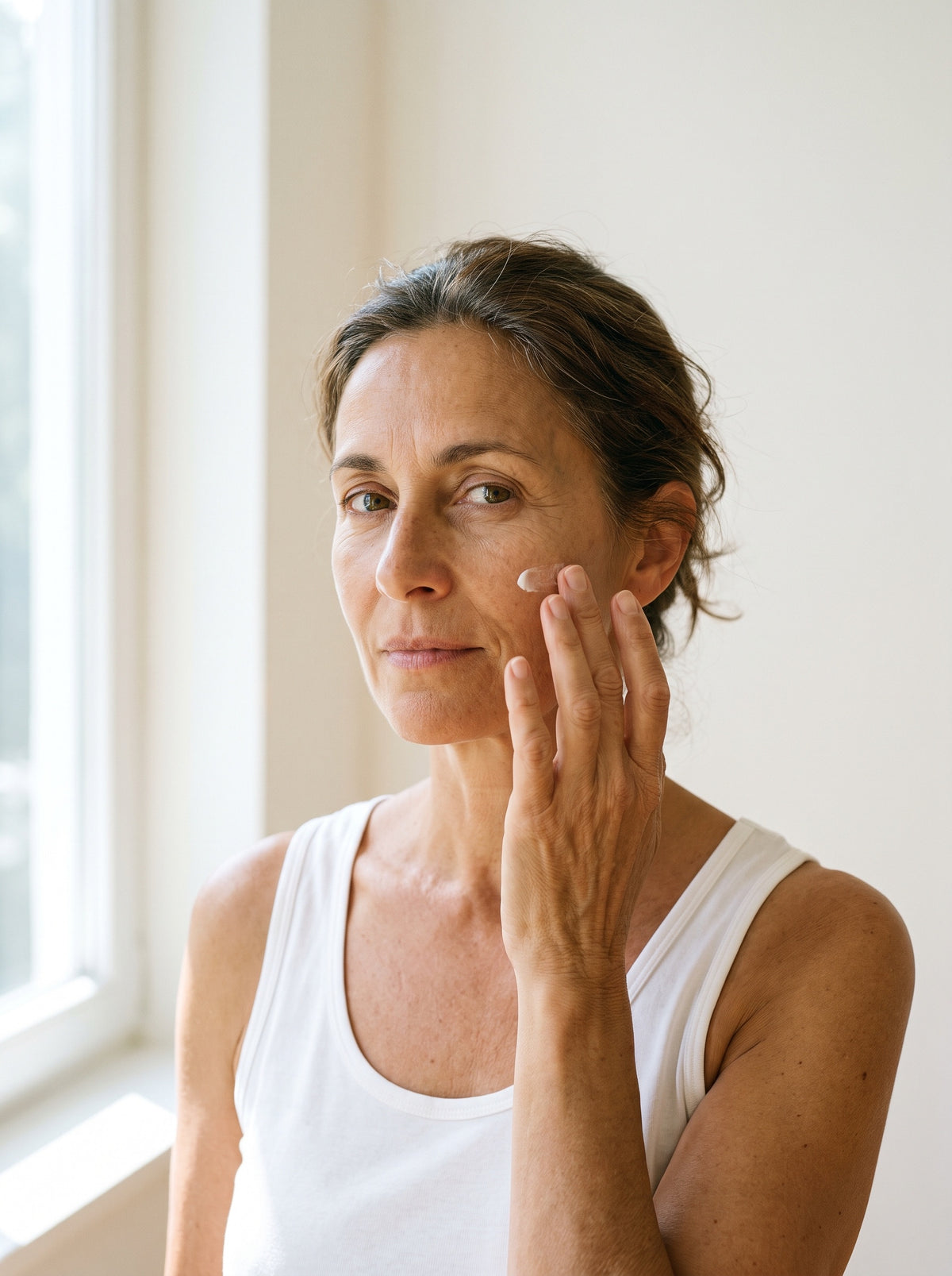 Illustrative portrait of a mature woman gently applying cream to her cheek